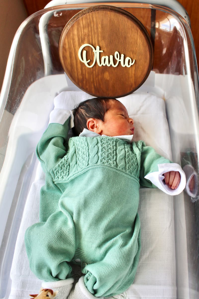 Newborn baby in a green knit outfit in a bassinet with a wooden name sign